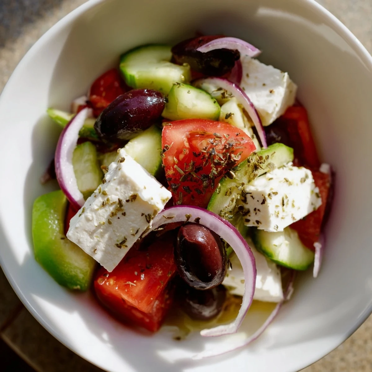 Colorful Greek Salad with Kalamata Olives and Feta Cheese in a white bowl, garnished with oregano and ready to serve as a light meal.