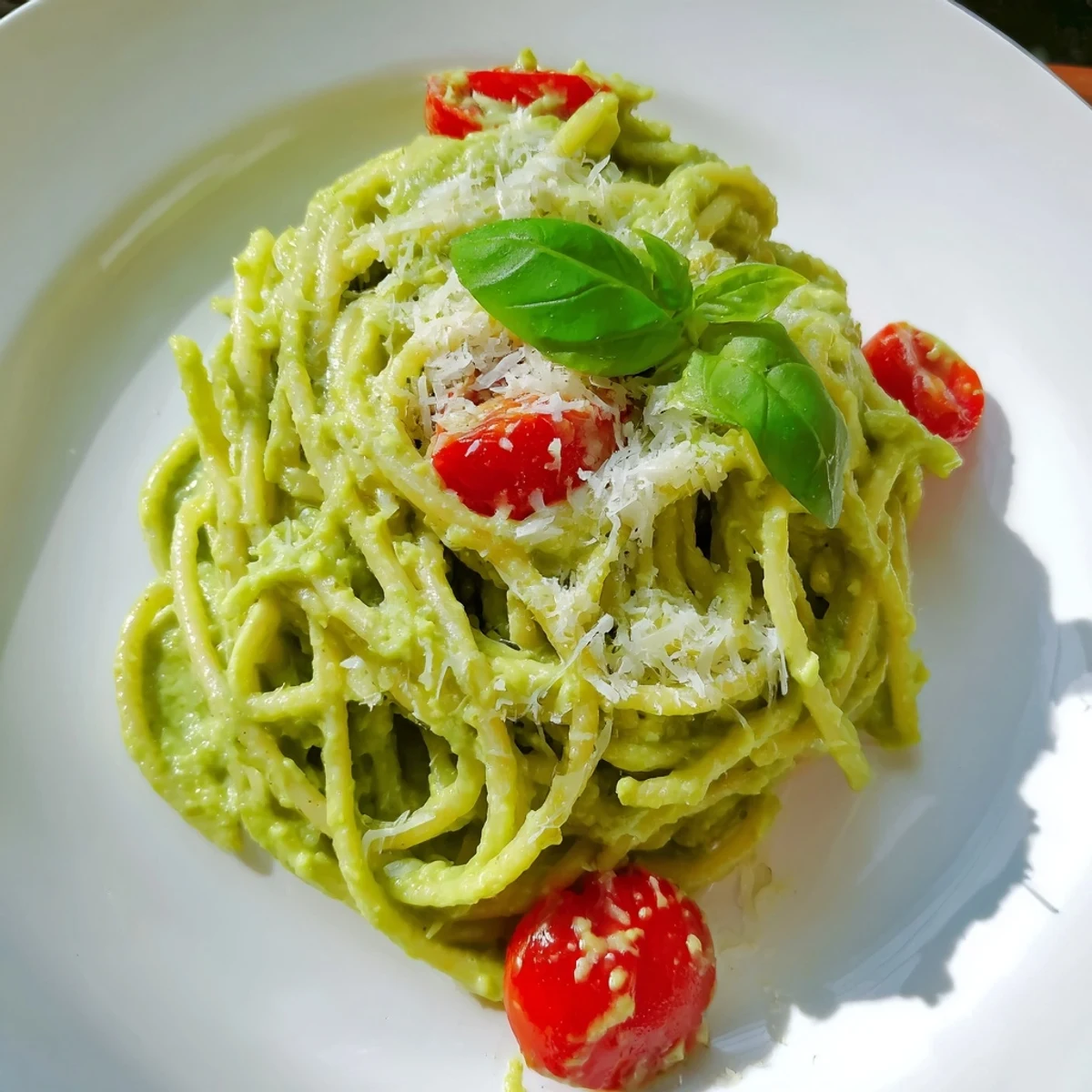 Creamy Avocado Lime Pasta with Cherry Tomatoes garnished with fresh basil and lime zest in a white bowl.