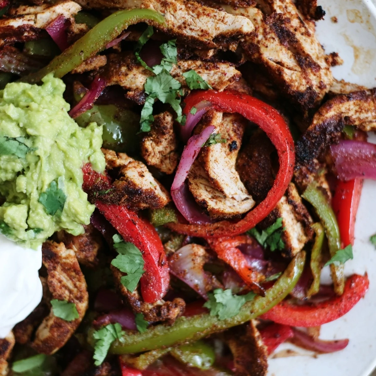 Juicy Sheet Pan Chicken Fajitas with Onions and Peppers plated with guacamole and salsa for a family dinner.