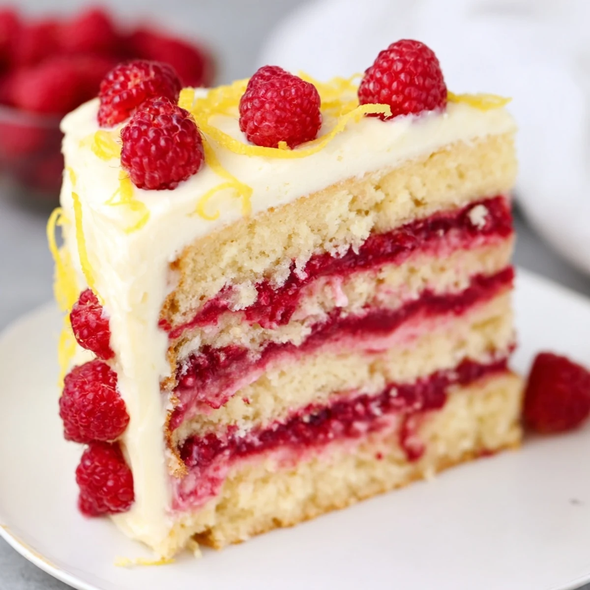 Freshly sliced Lemon Raspberry Layer Cake with silky buttercream on a white plate, ready to serve.