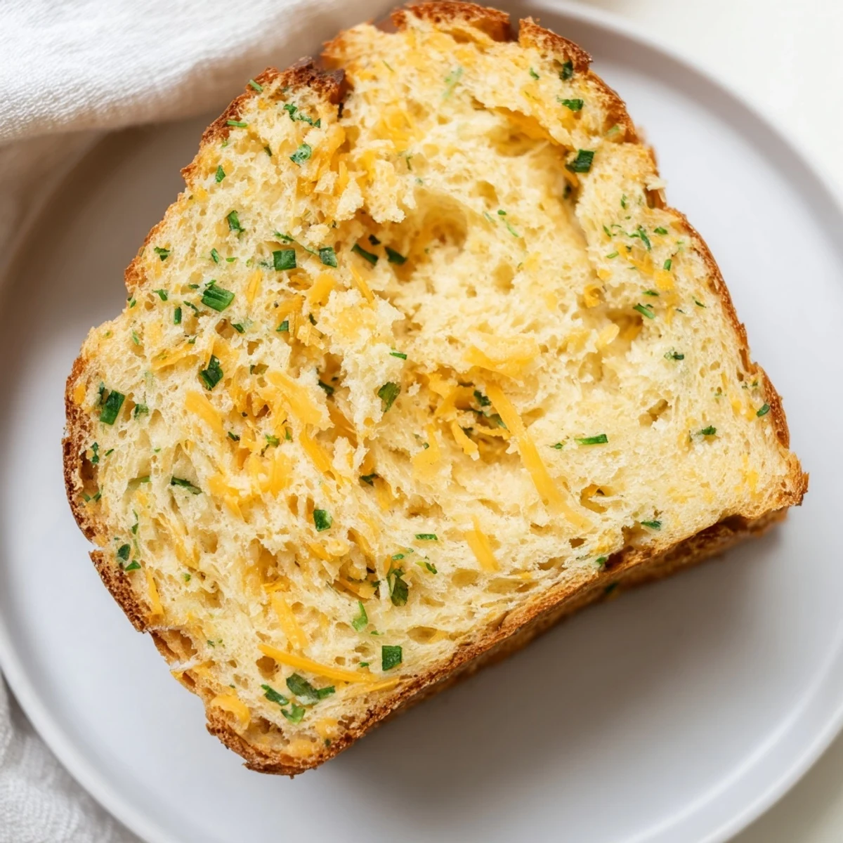 Slice of savory bread with cheese on a wooden cutting board, revealing moist crumb and pockets of melted sharp cheddar.  