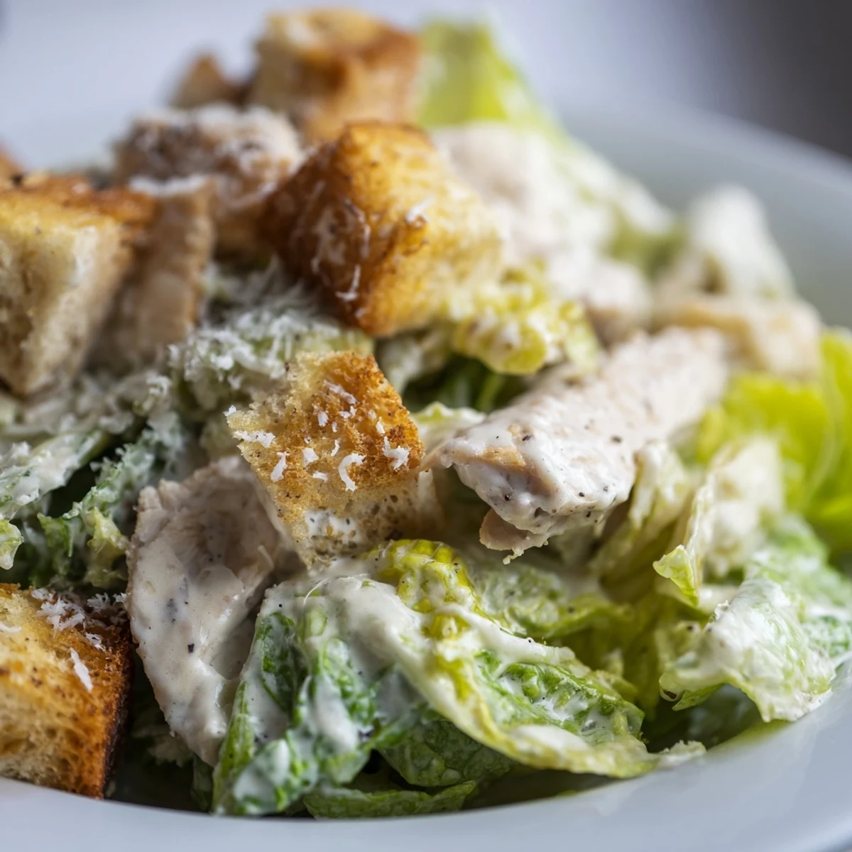 A creamy Caesar dressing coats the greens, with shaved Parmesan cheese visible.