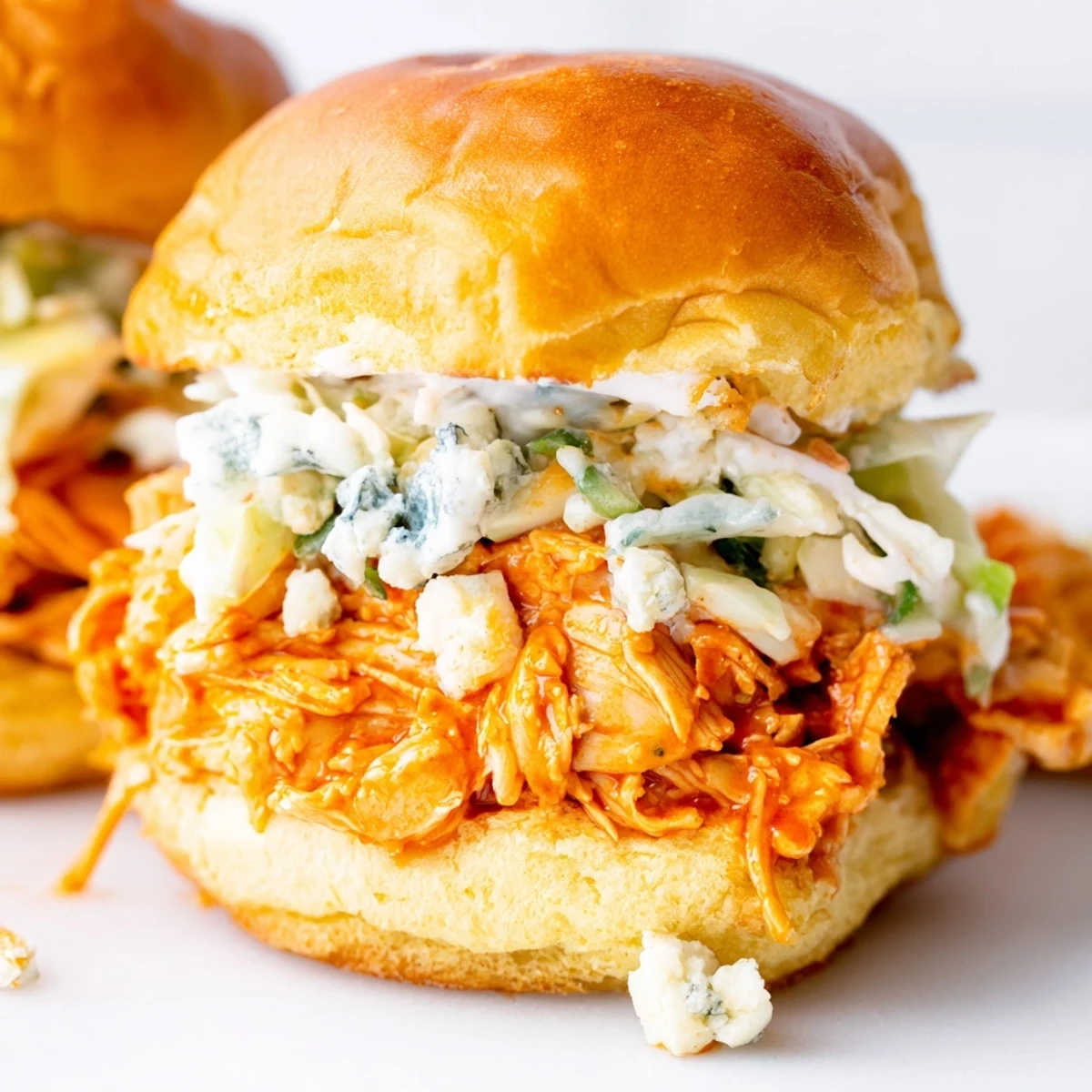 A close-up of warm buffalo chicken sliders topped with crumbled blue cheese and fresh chives on a game day table.