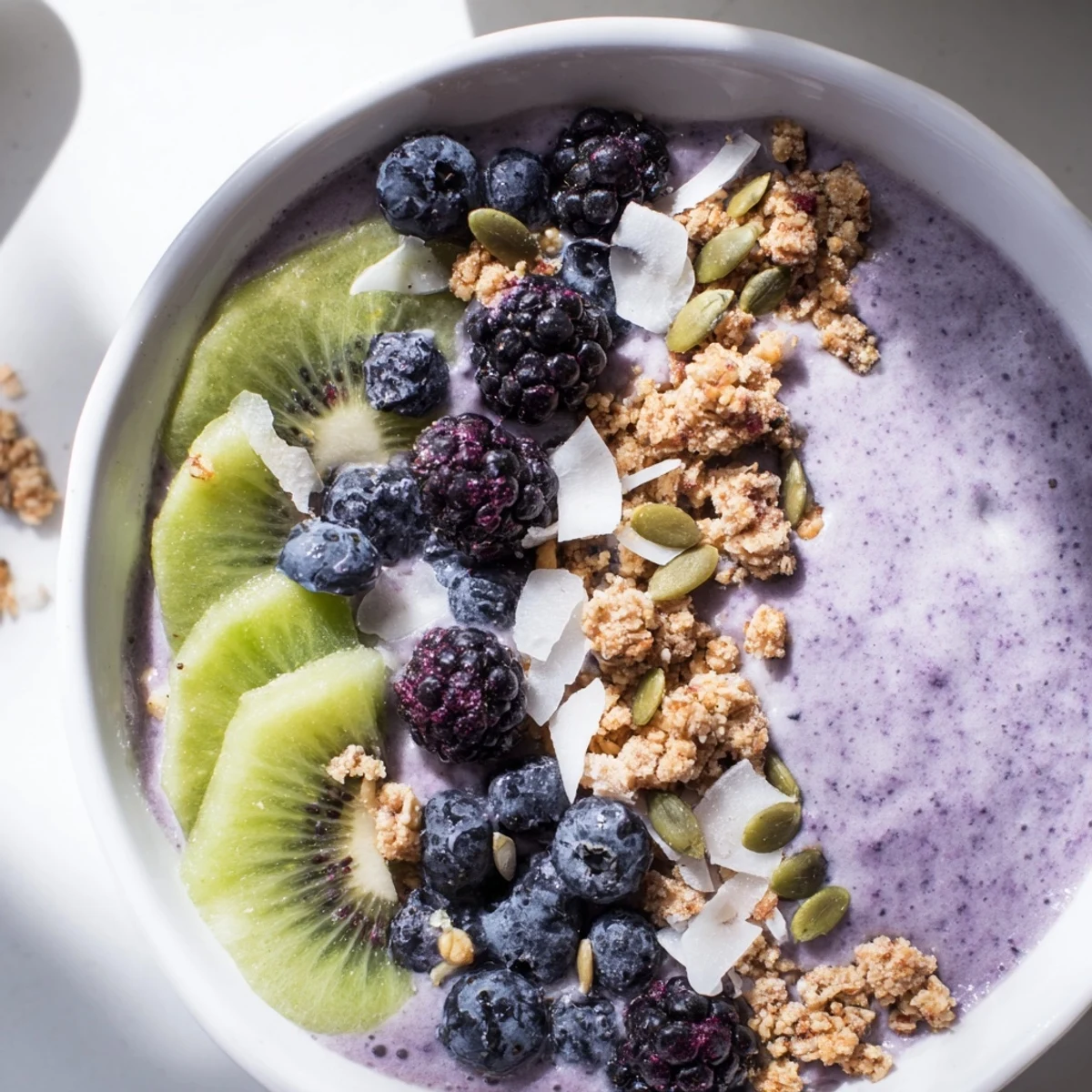 Thick, purple Winter Berry Smoothie Bowl with crunchy granola and fresh kiwi slices.  