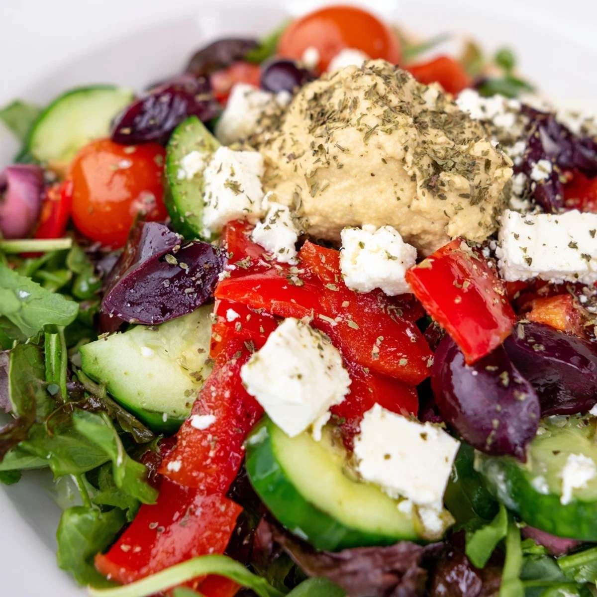 Fresh Mediterranean Salad with Hummus features crisp cucumber, juicy tomatoes, and crumbled feta on a bed of greens, crowned with a creamy dollop of hummus.