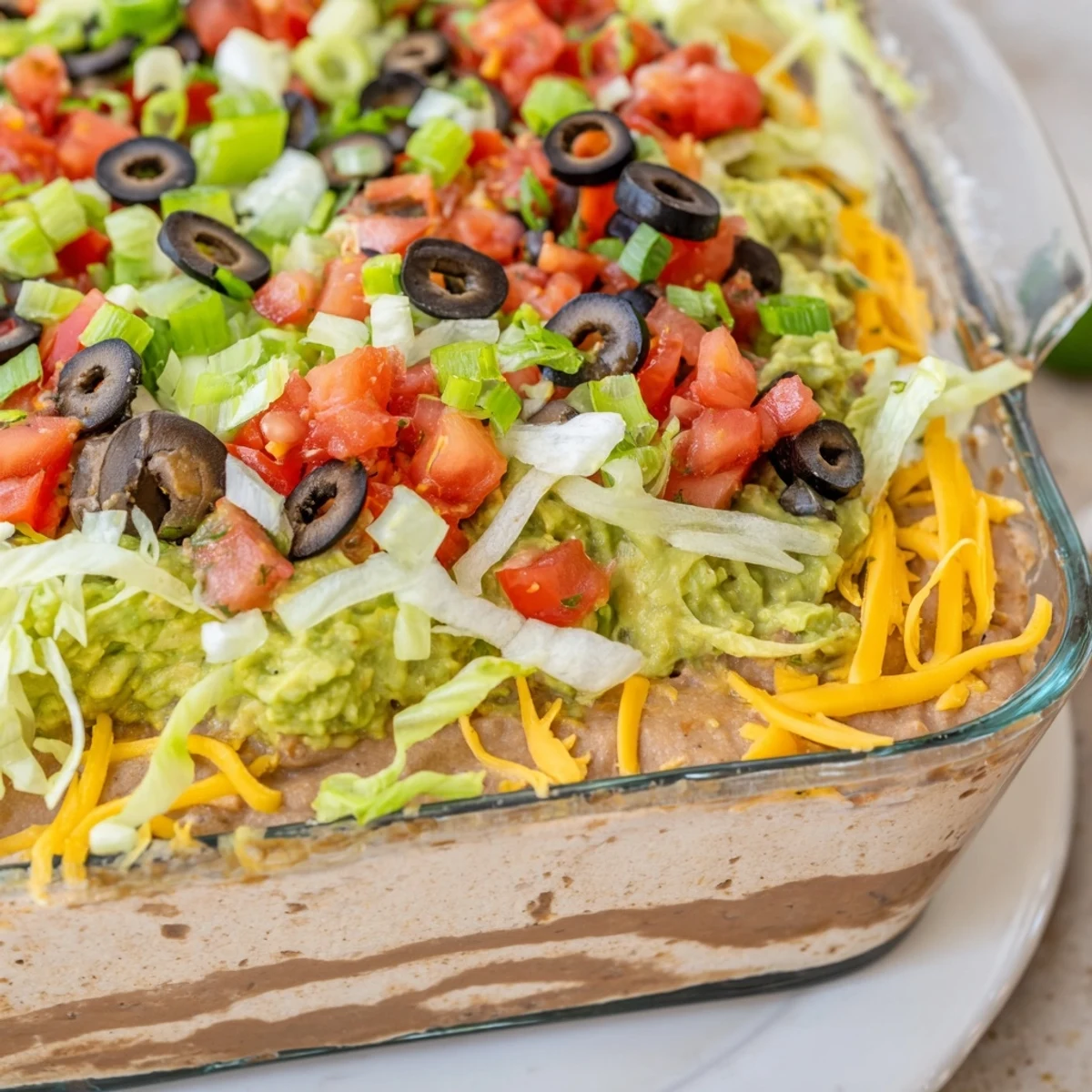 Seven Layer Taco Dip served in a glass dish with colorful toppings and tortilla chips for dipping. 