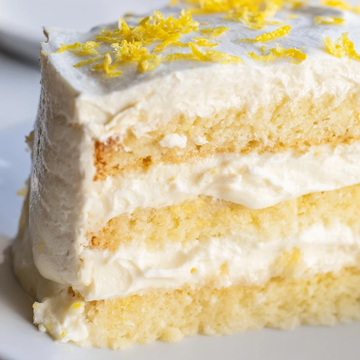 A slice of Limoncello Mascarpone Cake reveals airy sponge, tangy syrup, and velvety mascarpone frosting with lemon zest.