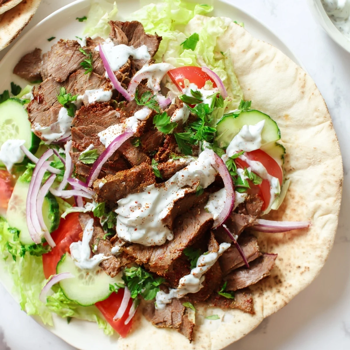 A close up view of a juicy Homemade Doner Kebab wrapped in pita with creamy white sauce drizzled over the top.