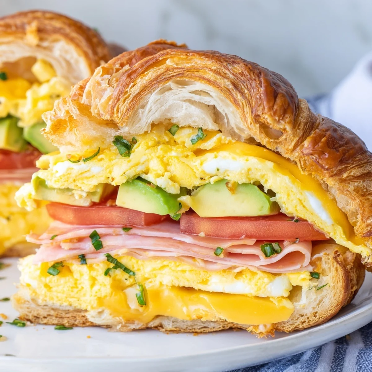 Buttery, flaky croissant breakfast sandwich topped with fresh chives and ripe avocado slices.