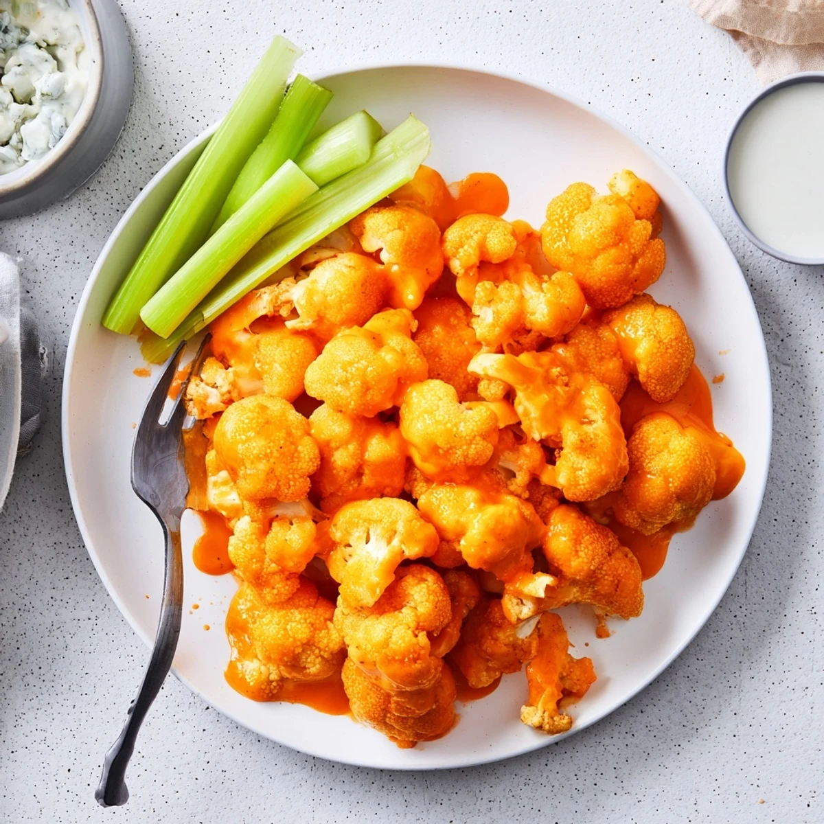 Golden crispy Air Fryer Buffalo Cauliflower florets glistening with tangy spicy sauce, served with fresh celery sticks and cool ranch dressing on a plate.