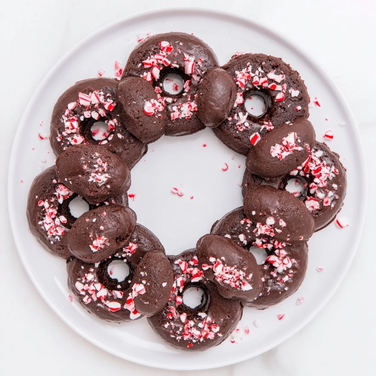 A close-up view shows a soft, chewy chocolate peppermint mochi donut with glossy glaze and sparkling red peppermint bits.