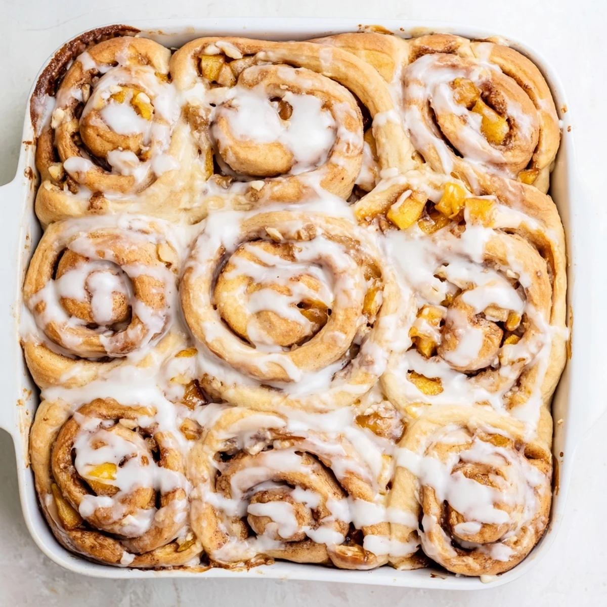 Golden peach pie cinnamon rolls drizzled with white icing on a serving plate