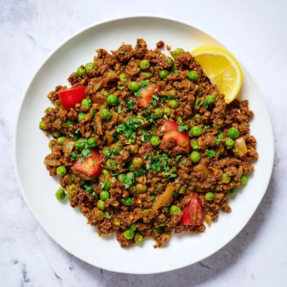 Golden savory Keema Curry with ground meat, green peas, and fresh cilantro garnish in a white bowl