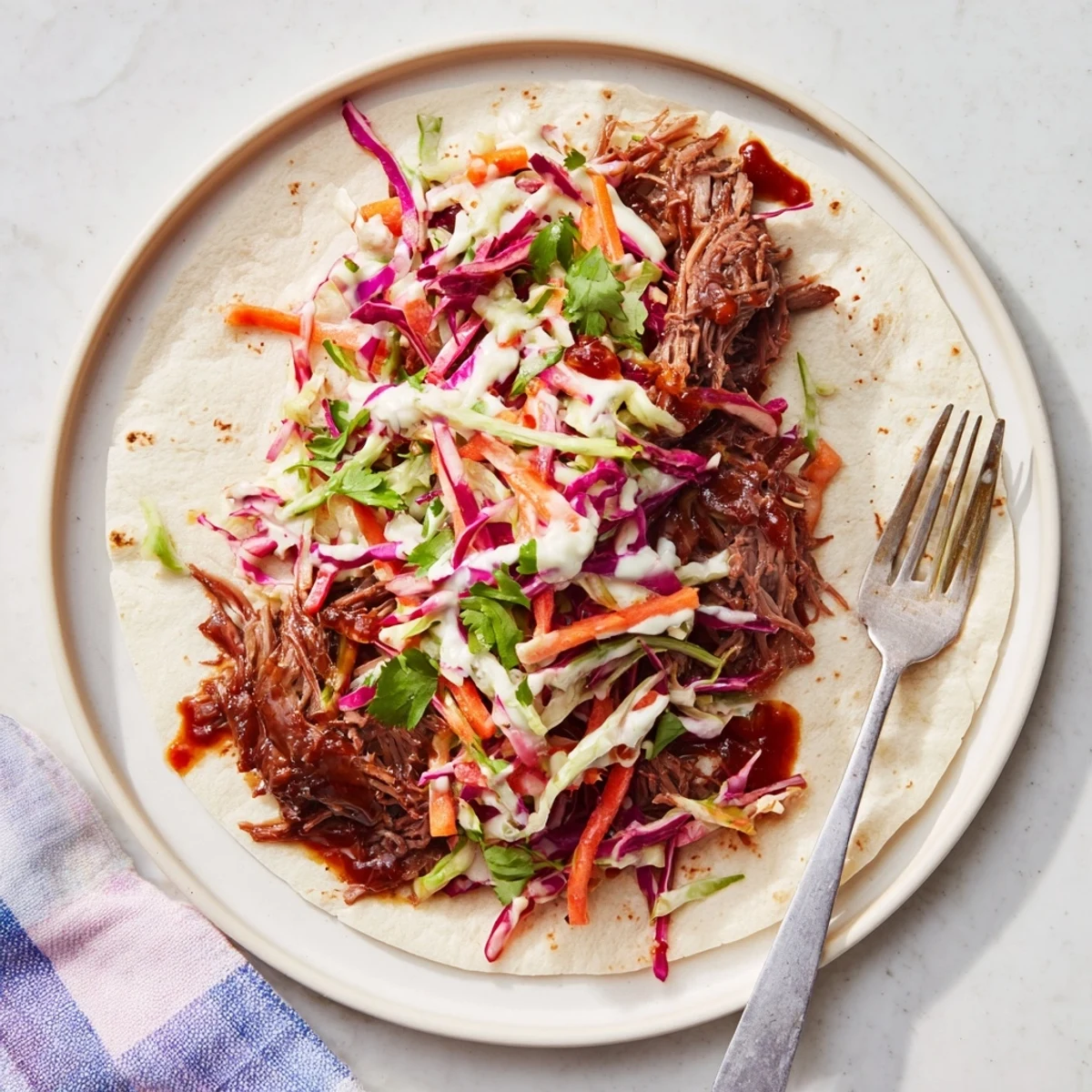 Tender smoky BBQ pulled beef wrapped in soft flour tortillas topped with colorful crunchy cabbage slaw