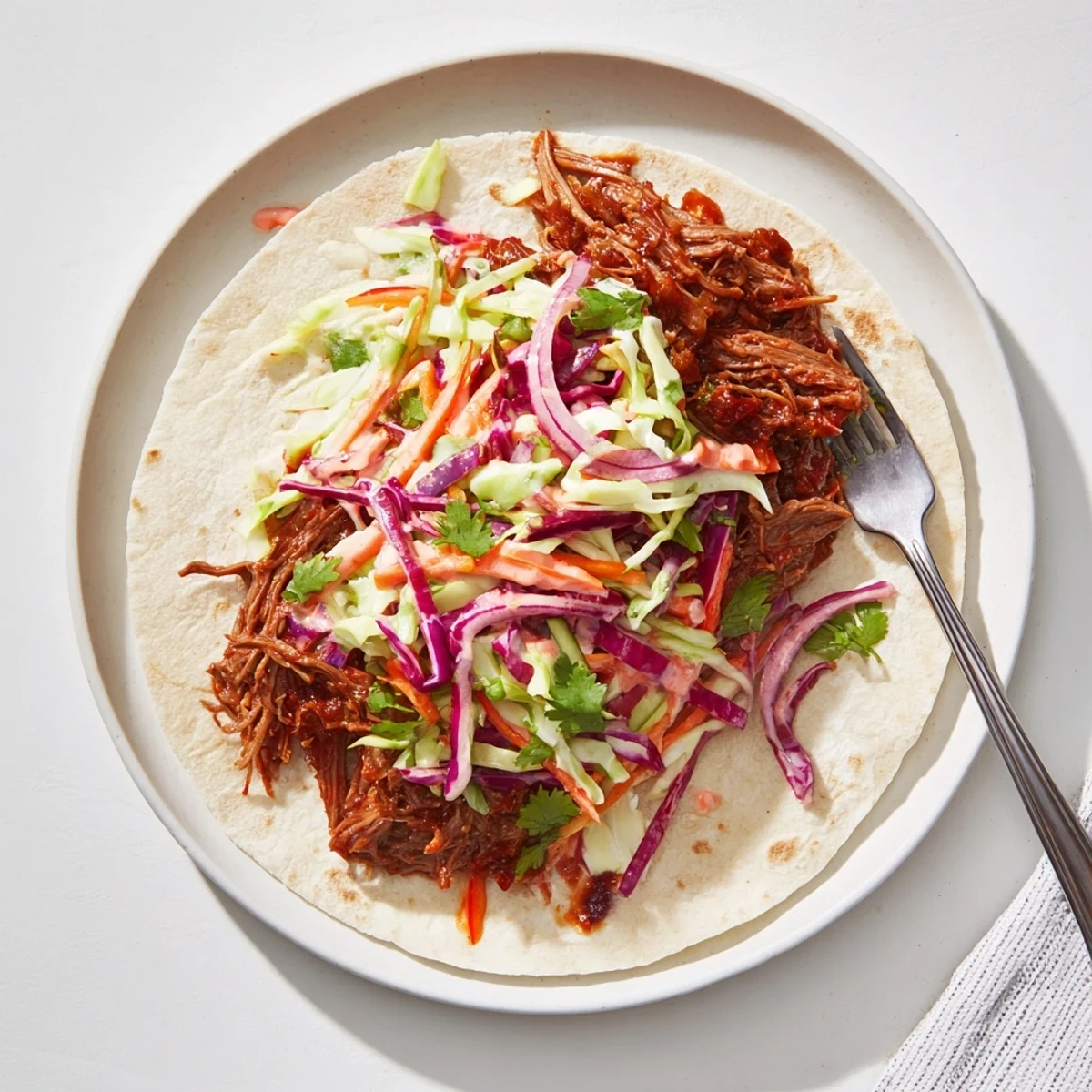 Homemade BBQ pulled beef wraps with vibrant red and green cabbage slaw in warm flour tortillas