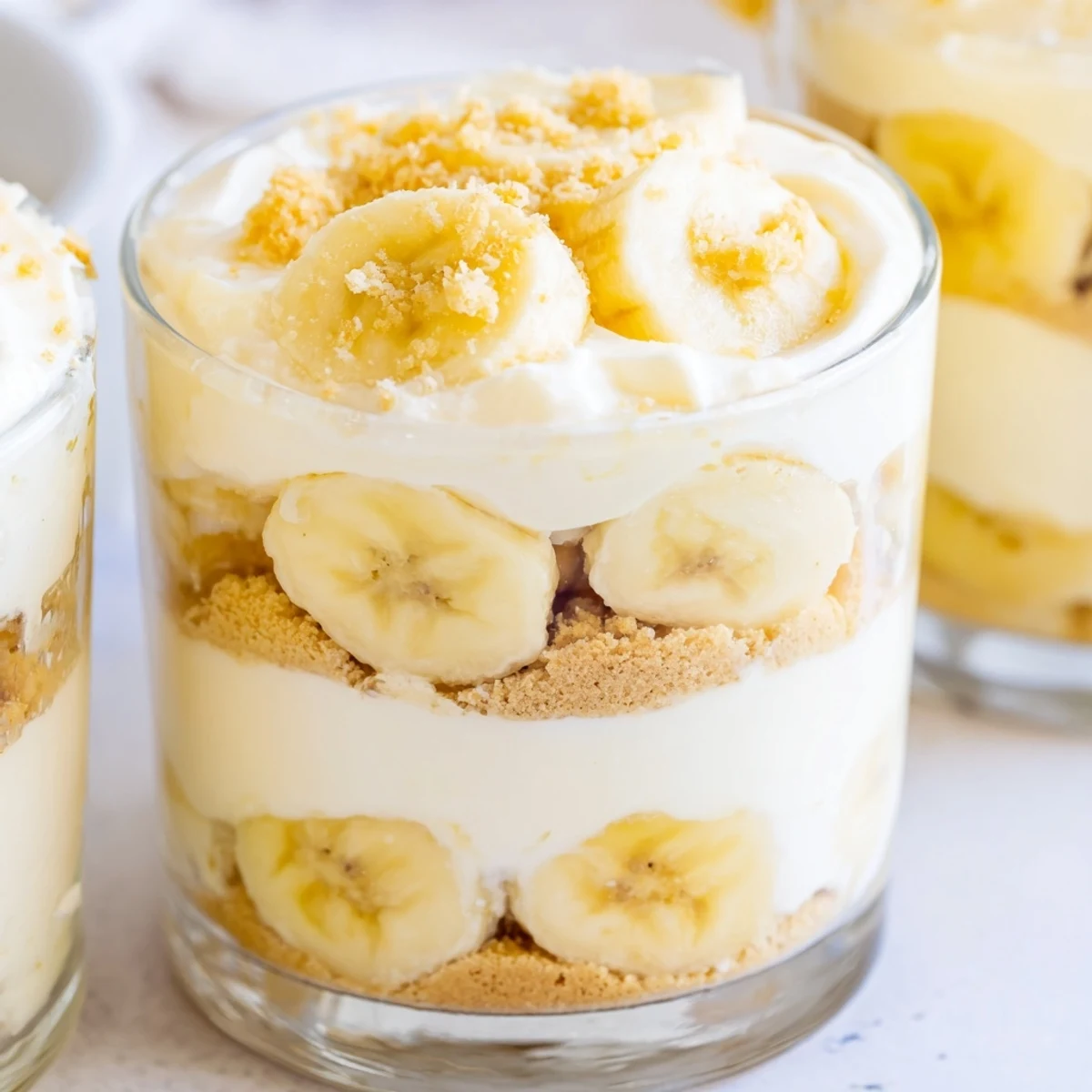 Creamy no bake banana pudding cheesecake cups topped with fresh banana slices and wafer crumbs