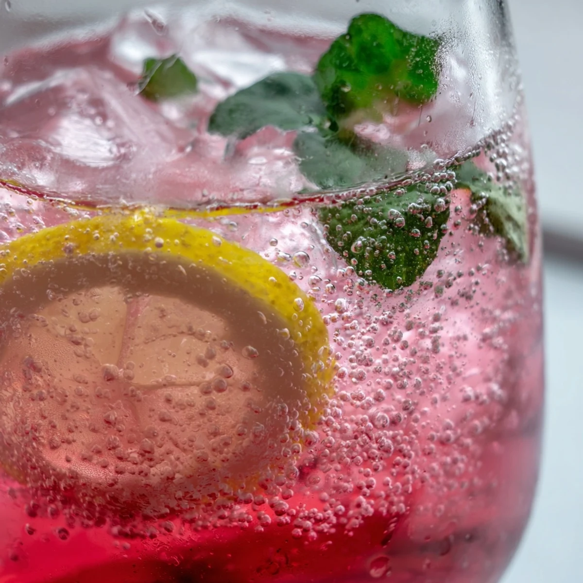 Sparkling pink lemon soda with honey served over ice on a sunny patio table