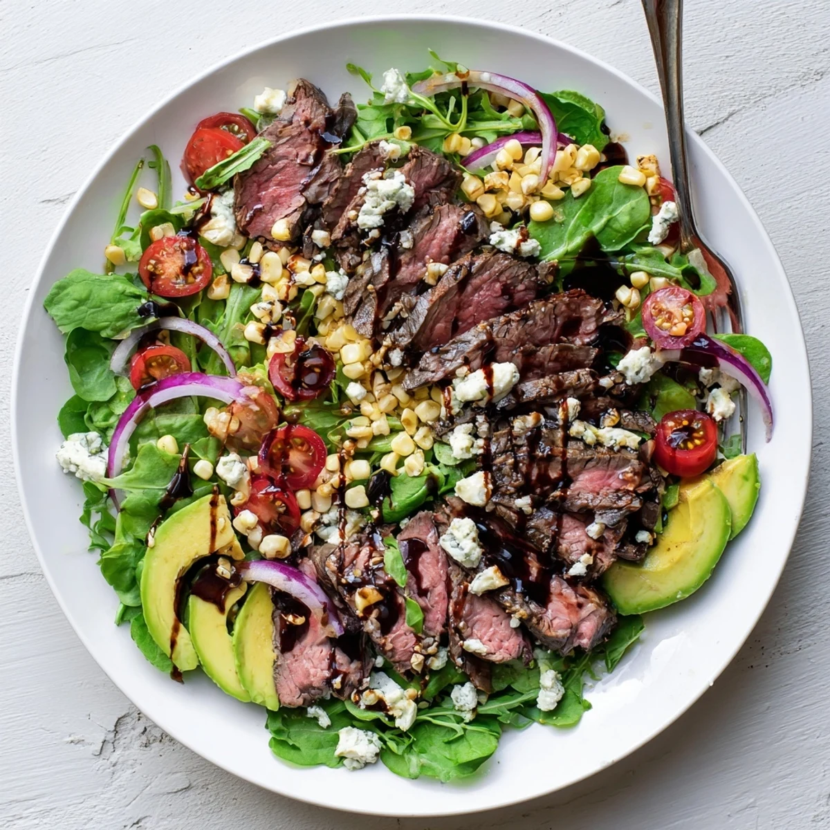 Sliced balsamic steak gorgonzola salad with charred corn on a white platter