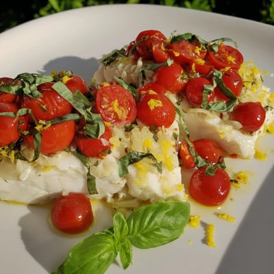 Golden-baked halibut topped with juicy cherry tomatoes, fresh basil, and shallots, served alongside roasted asparagus on a white plate.