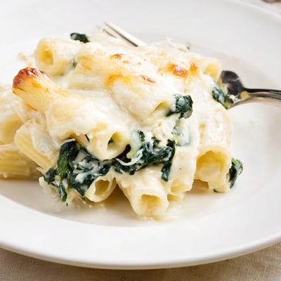 Creamy Spinach and Cheese Pasta Bake served in a white dish with a wooden spoon.