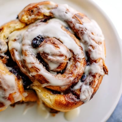 Freshly baked Blueberry Cinnamon Rolls with swirls of blueberries, cinnamon sugar, and a sweet glaze on a white plate.  