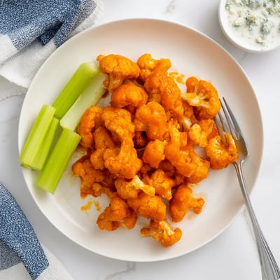 Air Fryer Buffalo Cauliflower bites with a crunchy golden coating, tossed in vibrant red buffalo sauce and arranged beside blue cheese dip and celery.