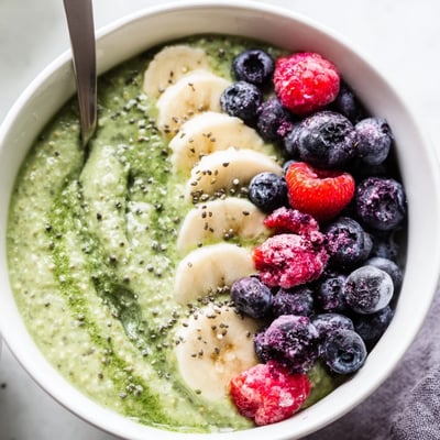 Vibrant green Matcha Protein Overnight Oats with nuts and coconut on a marble counter.